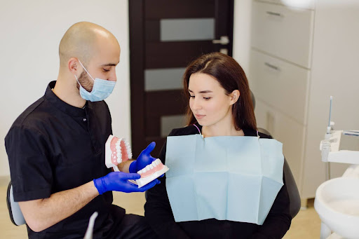 A dentist is explaining a procedure to a patient using a tooth model.