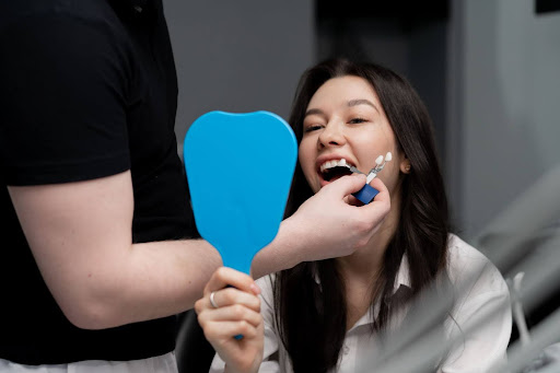 A patient is holding up a mirror while the dentist is finding the best tooth shade to match.