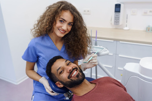 The female dentist smiles after examining a multiracial man’s teeth for possible filling needs.