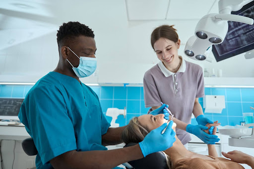 A dentist performs a dental exam on his patient with her partner holding her hand.