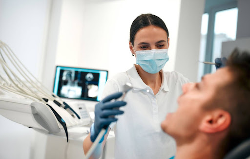 Female dentist wearing a mask prepares to clean a male patients teeth with a dental X-ray visible behind them